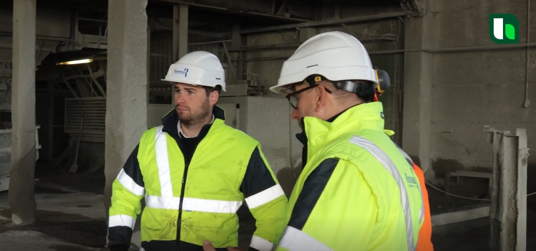Two workers in safety gear and helmets discuss inside an industrial facility.