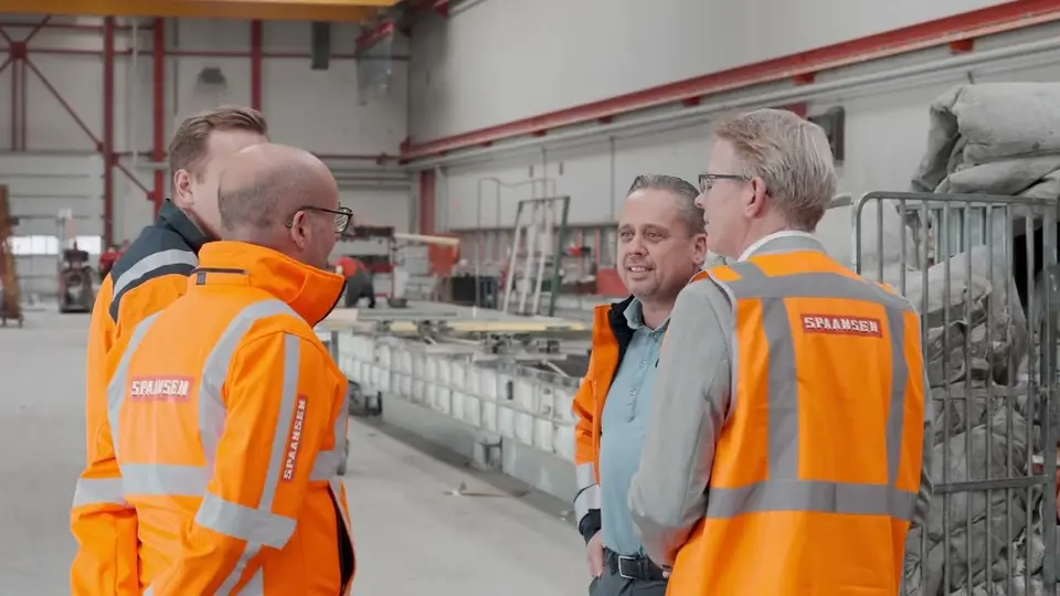Four people in safety vests having a discussion inside an industrial facility.
